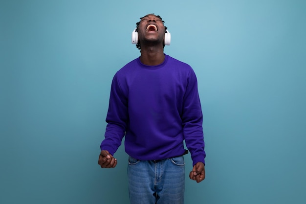 African young guy in a blue sweatshirt listens to music with headphones