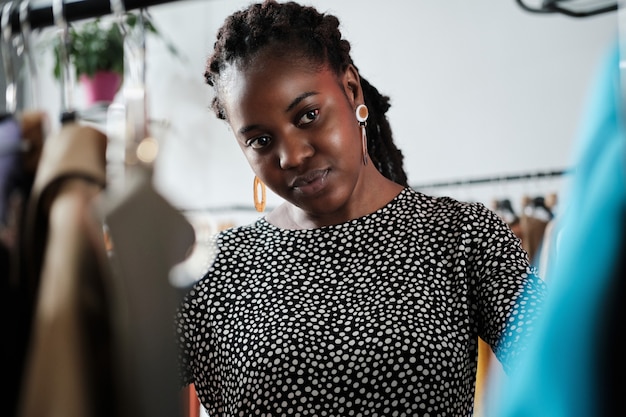 African young woman choosing new clothes for herself on the rack during shopping