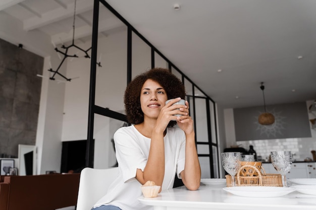 African young woman is eating breakfast and getting boost of energy for the whole day African american girl is drinking coffee and tasting cake at the dinner table Cozy morning lifestyle