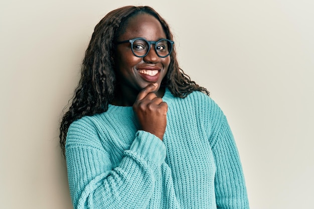 African young woman wearing casual clothes and glasses smiling looking confident at the camera with crossed arms and hand on chin. thinking positive.