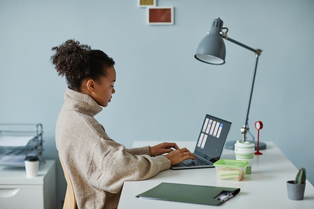 African young woman working with online project on laptop sitting at her workplace at office