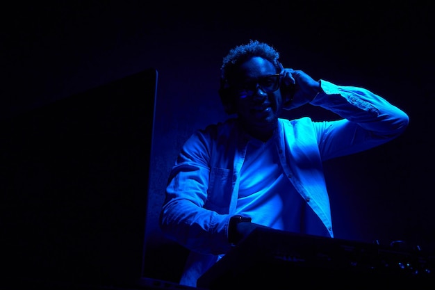 AfricanAmerican DJ with headphones is sitting in a dark studio