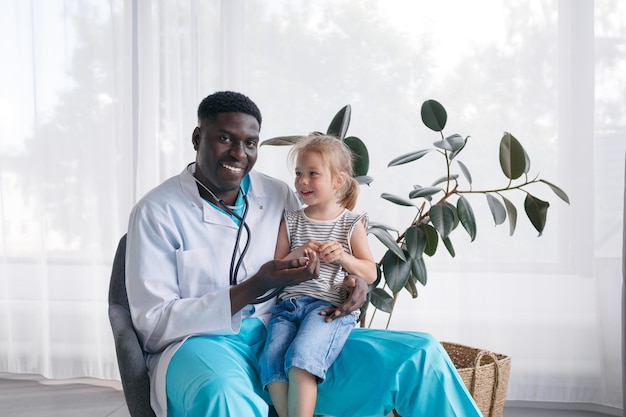 An AfricanAmerican doctor communicates with a little girl patient who is sitting on the doctor's lap