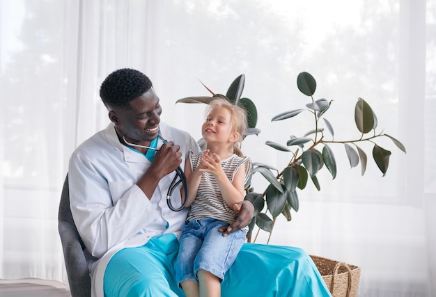 An AfricanAmerican doctor communicates with a little girl patient who is sitting on the doctor's lap