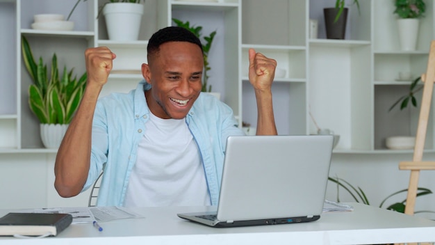 AfricanAmerican feels happy received great news by internet looks at pc screen raised hands scream with joy celebrating online lottery win