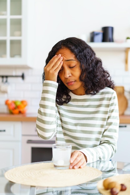 Africanamerican female dealing with headache dissolving pill in glass of water