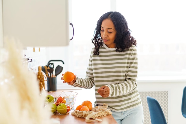 Africanamerican female in kitchen sorting out apples and oranges after shopping in grocery store