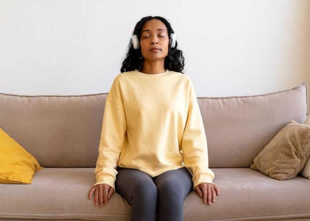 Africanamerican female sitting on couch and listening to music in headphones breathing therapy