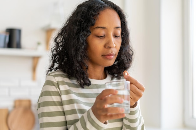 Africanamerican female washing down pill with glass of waterhealthy supplement remedy treatment