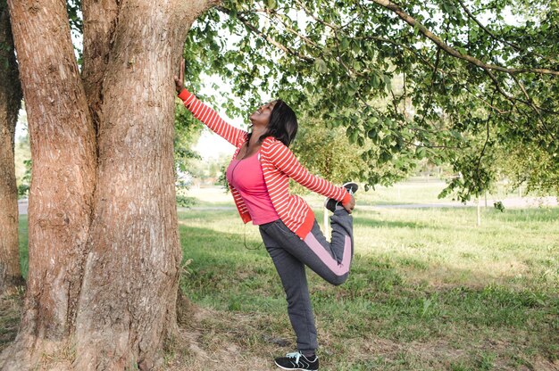 An AfricanAmerican girl doing sports performed a warmup while holding a tree with her hand