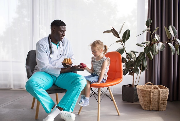 An AfricanAmerican nutritionist communicates with a small patient and offers a fresh apple