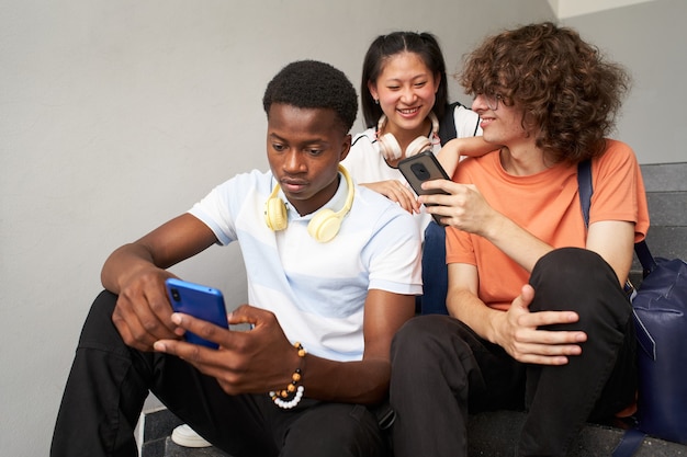 An africanamerican student chats alone and his classmates laugh as they use their cell phones