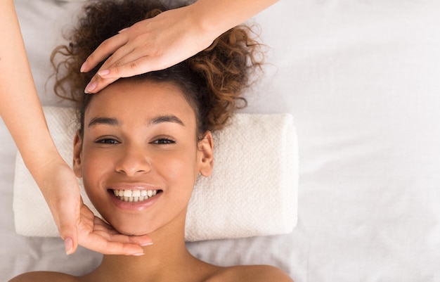 Africanamerican woman enjoying face massage at beauty salon