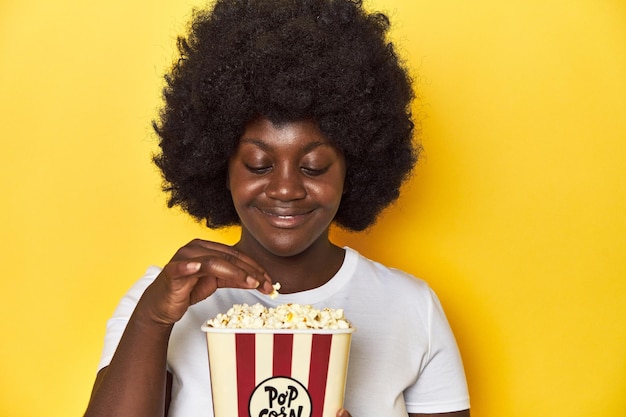 AfricanAmerican woman holding popcorn cinema concept on a yellow background