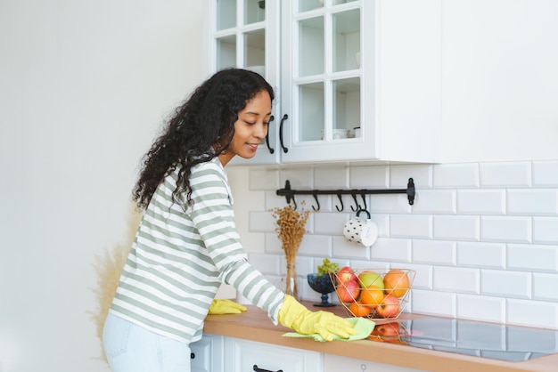 Africanamerican woman in rubber gloves occupied with household duties in kitchen