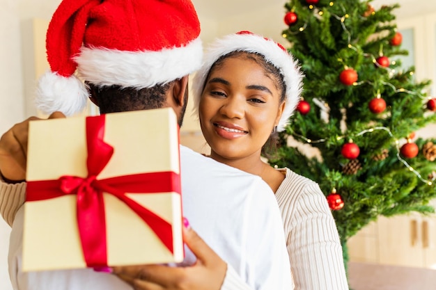 Afro american couple giving gift box to each other in house near christmas tree