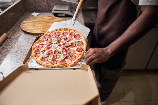 Afro American male hand transferring delicious freshly baked pizza with metal peel