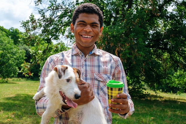 Afro american man holds a jack russell dog and drinks coffee from a paper cup