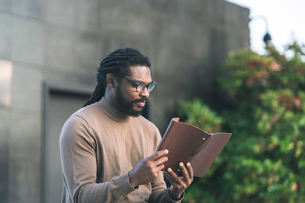 Afro american man with glasses reading in a park