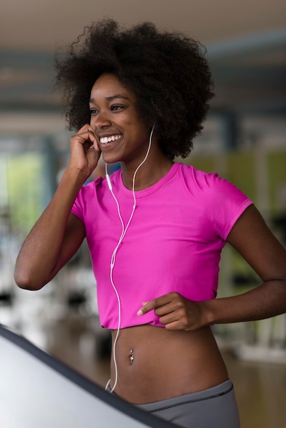 afro american woman running on a treadmill at the gym while listening music on earphones