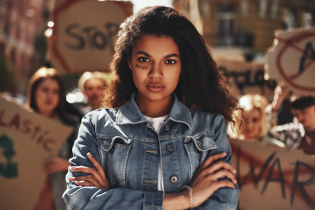 Afro american woman with word power written on her face keeping arms crossed and protesting