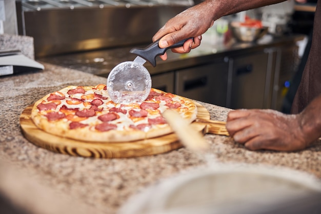 Afro American young man slicing pizza with round cutter wheel