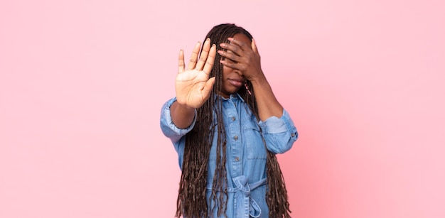 Afro black adult woman covering face with hand and putting other hand up front to stop camera, refusing photos or pictures