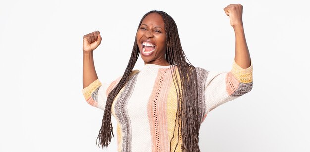 Afro black adult woman shouting triumphantly, looking like excited, happy and surprised winner, celebrating