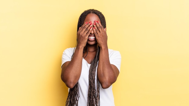 Afro black pretty woman covering face with hands, peeking between fingers with surprised expression and looking to the side