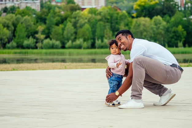 Afro father walking the first steps of his mixed race daughter spending time in garden