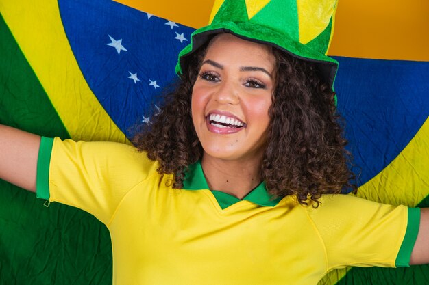 Afro girl cheering for favorite brazilian team, holding national flag in yellow background.