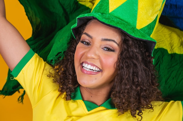 Afro girl cheering for favorite brazilian team, holding national flag in yellow background.