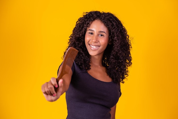 Afro girl with curly curly hair holding a comb on yellow background smiling at camera