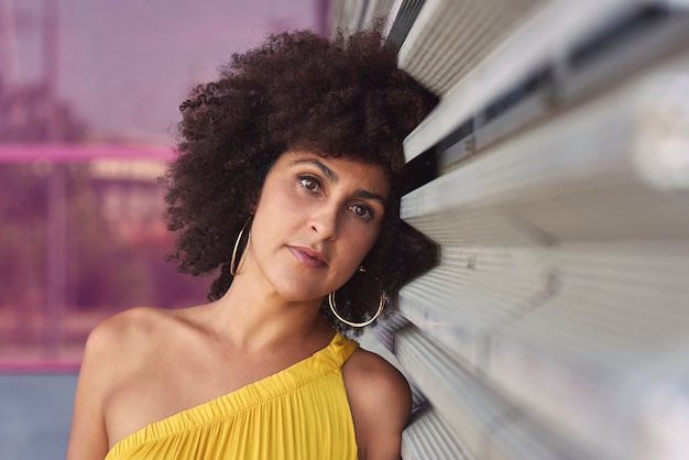 Afro-haired mulatto woman in a yellow dress and purple background.