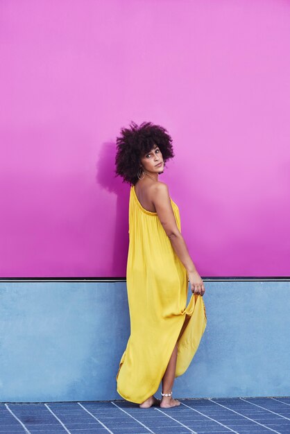 Afro-haired mulatto woman in a yellow dress and purple background.