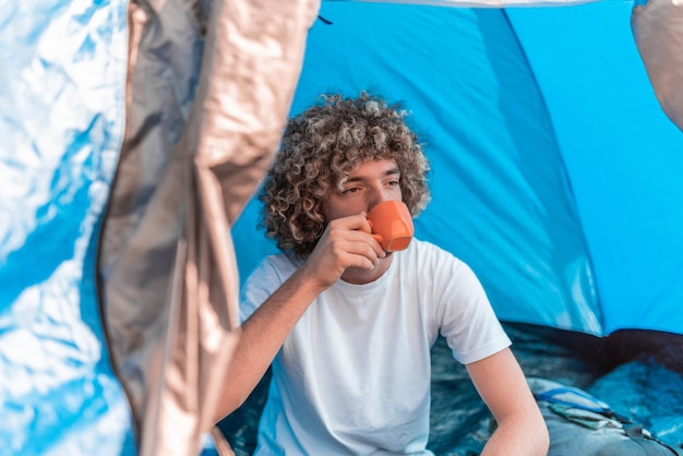 An Afro man drinks his morning coffee while sitting inside a mountain tent