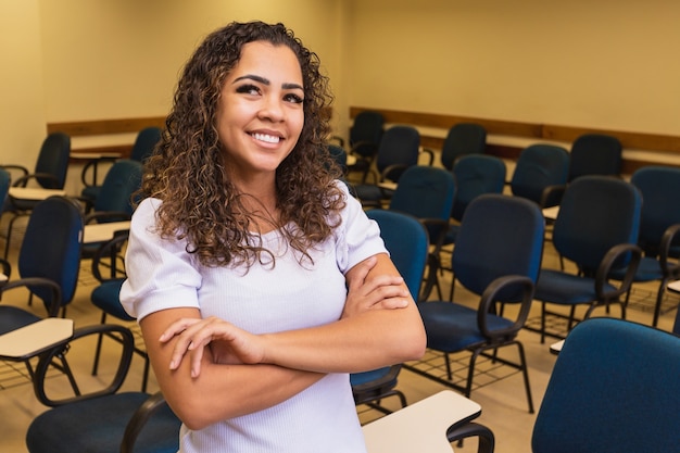 Afro student in classroom with arms crossed looking at camera smiling. Young student with the classroom in the background.