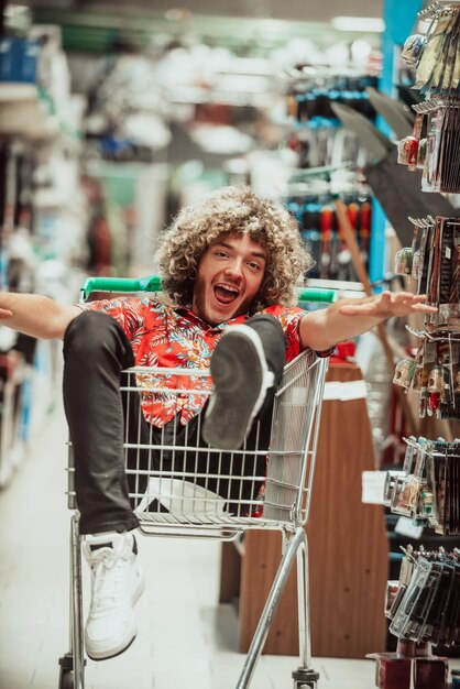 An afro teenager with a crazy face is sitting in a trolley in a big shopping mall. Fun shopping. High quality photo