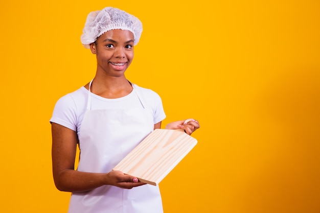 Afro woman in apron holding a meat board with space for text.