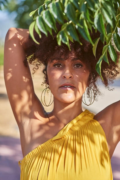 Afro woman holds some branches near her face. The shadow of the leaves is cast on his face. Ecology, nature concept.