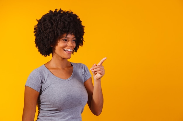 Afro woman pointing on yellow with space for the text