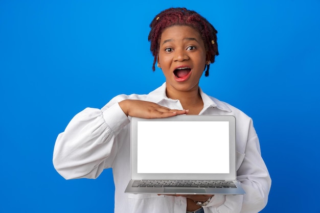 Afro woman showing laptop with blank white screen against blue background