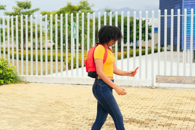 Afro woman walking and reading a text message on her cell phone