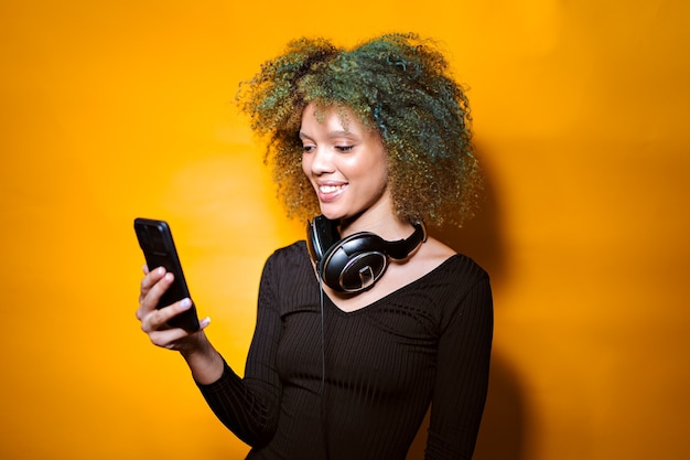 Afro woman with mobile phone and headphones on yellow background