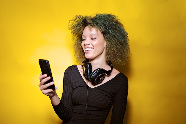 Afro woman with mobile phone and headphones on yellow background