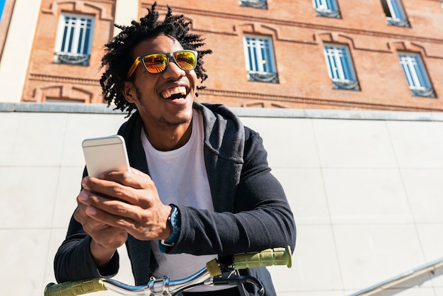 Afro young man using mobile phone and fixed gear bicycle in the street.