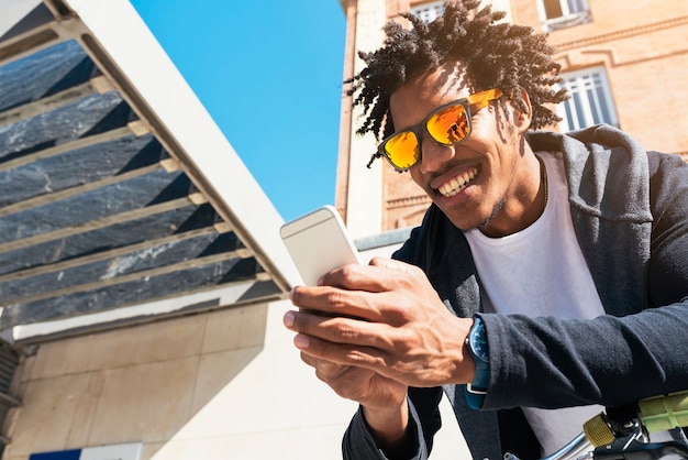 Afro young man using mobile phone and fixed gear bicycle in the street.