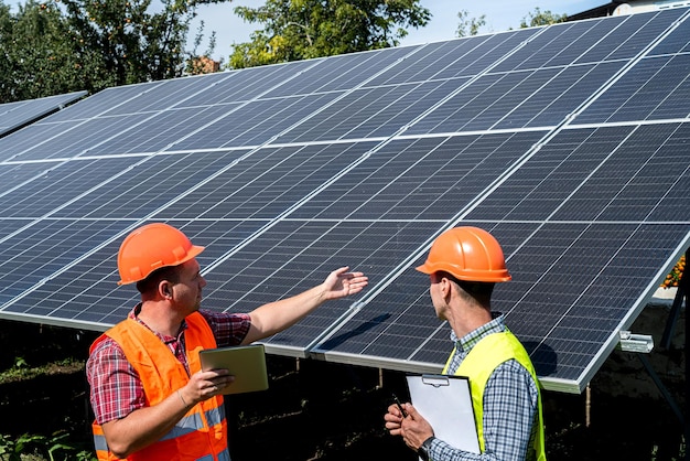 Against the background of solar panels two workers write in a tablet plan of work performed