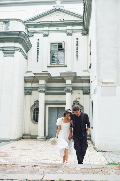 Against big church building Beautiful bride with his fiance is celebrating wedding outdoors