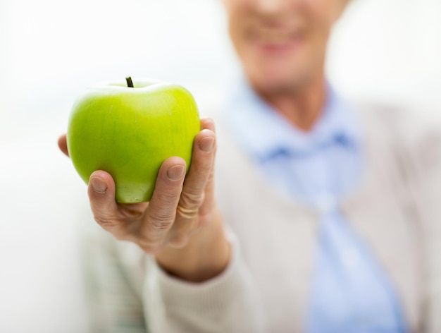 age, healthy eating, food, diet and people concept - close up of happy smiling senior woman with green apple at home